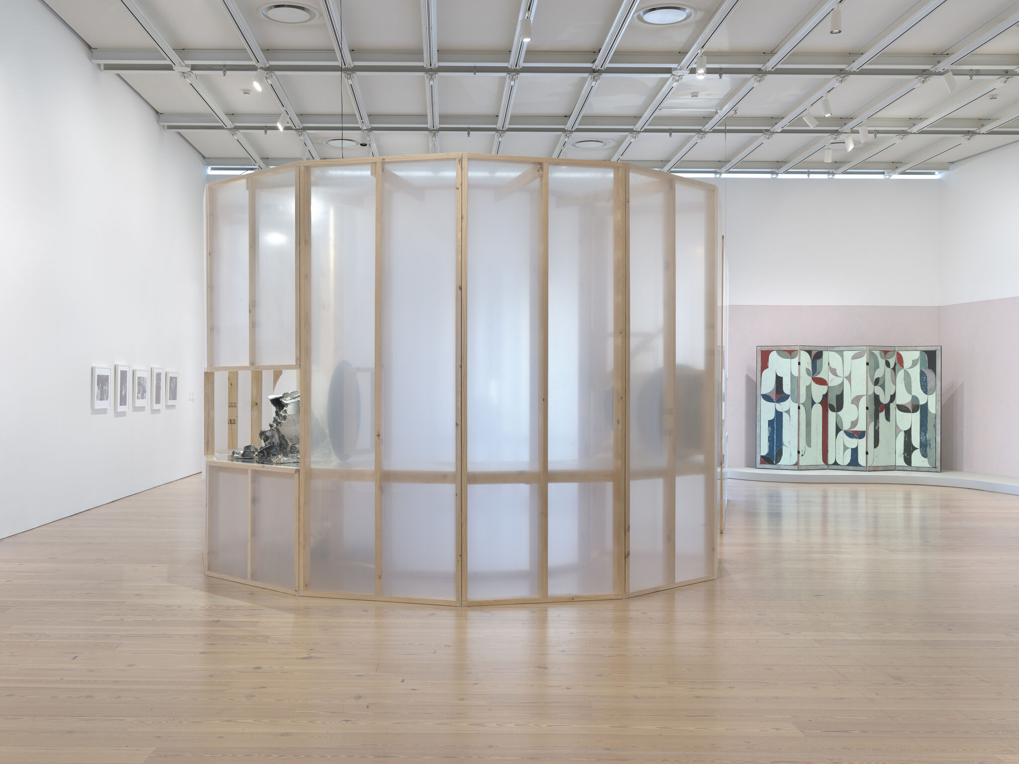 A big room with a white plastic and wood sculpture fixture in the middle. In th e back on the wall, there is a painting on a folding-panel.