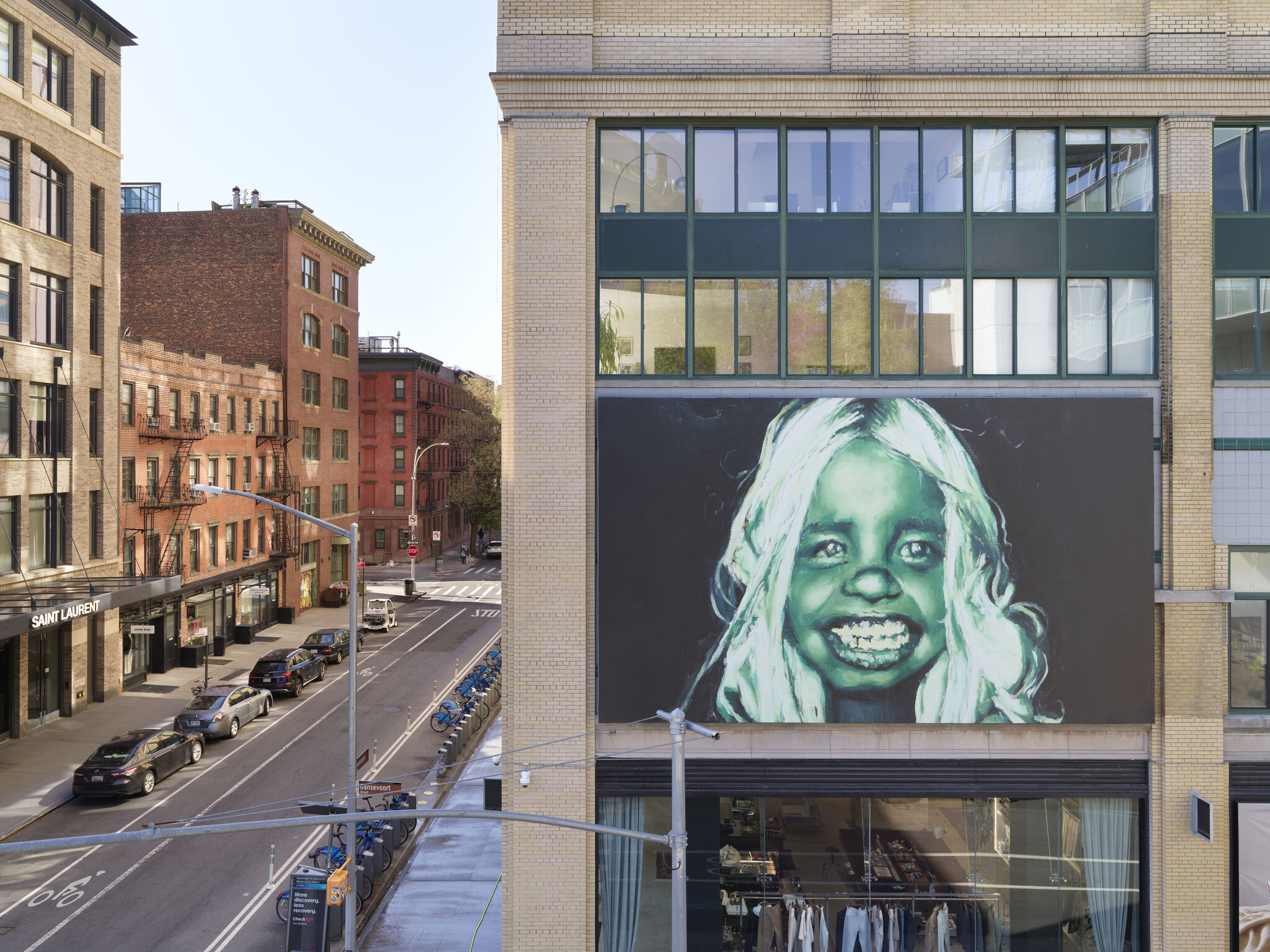 A large green painted smiling face mural covers a building wall above a city storefront.