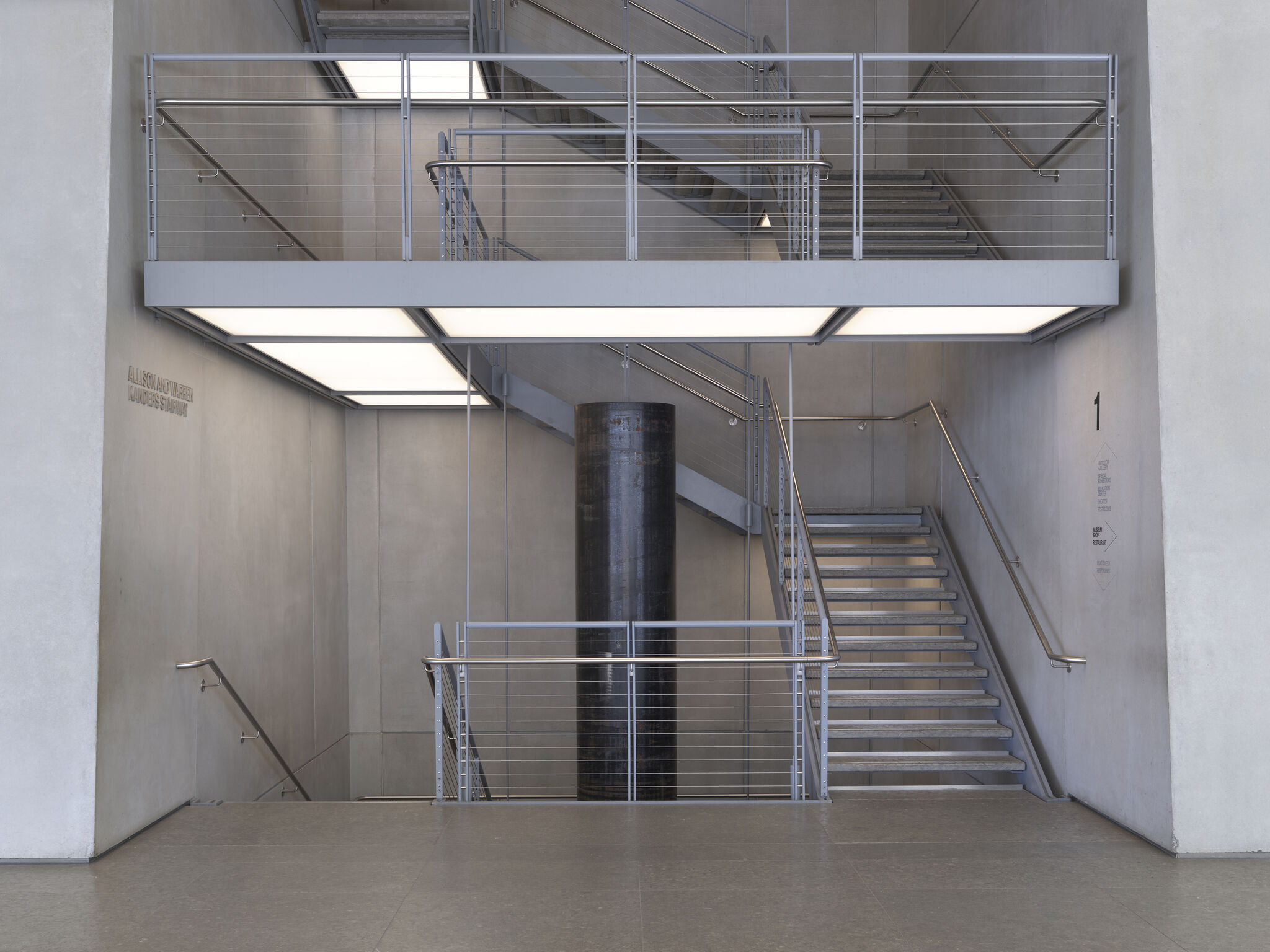 Metal stairwell with cable railings and lit ceiling panels inside a minimalist concrete interior.