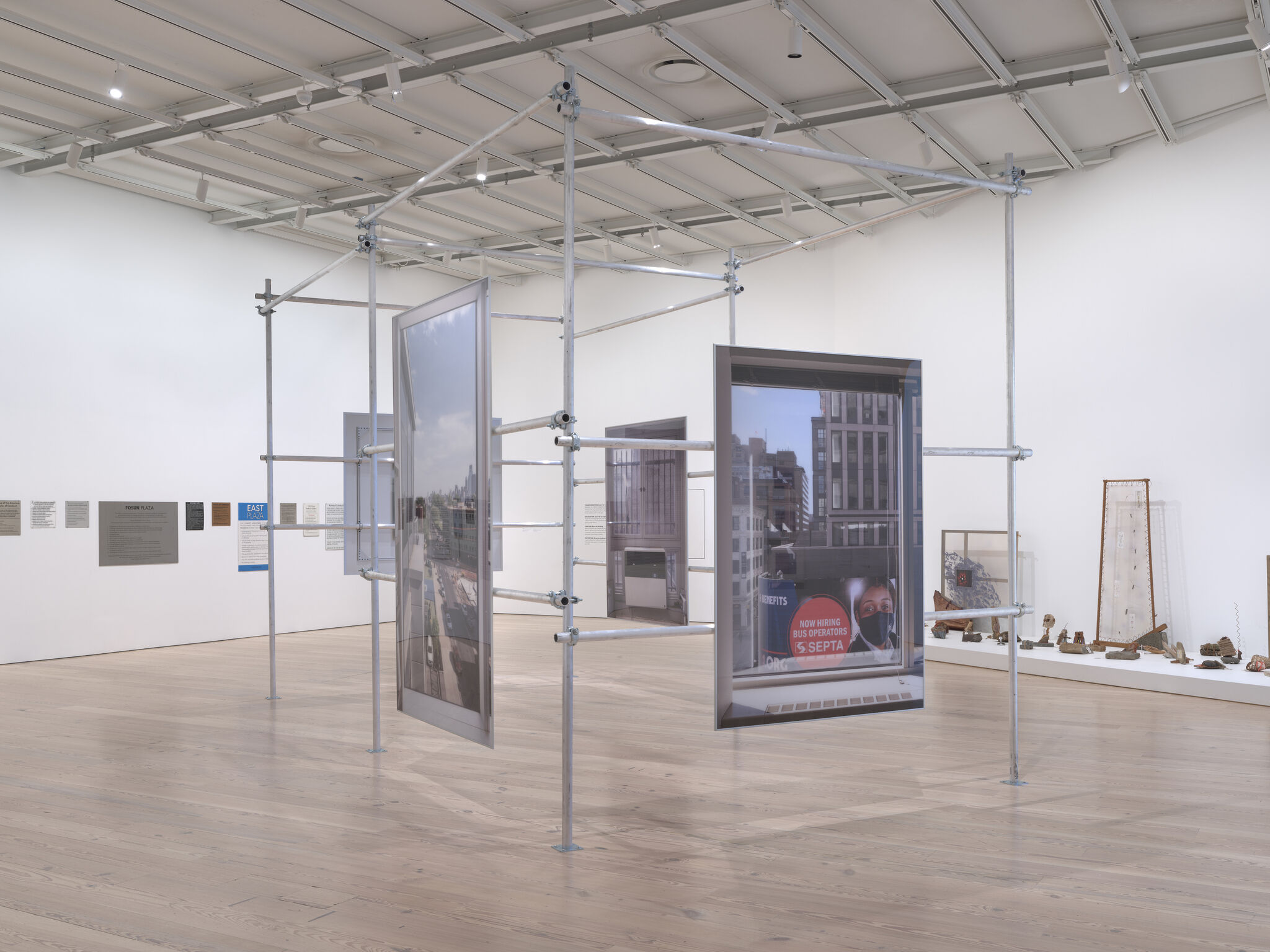 Metal scaffolding structure displays large framed photographs hanging in a bright museum gallery.