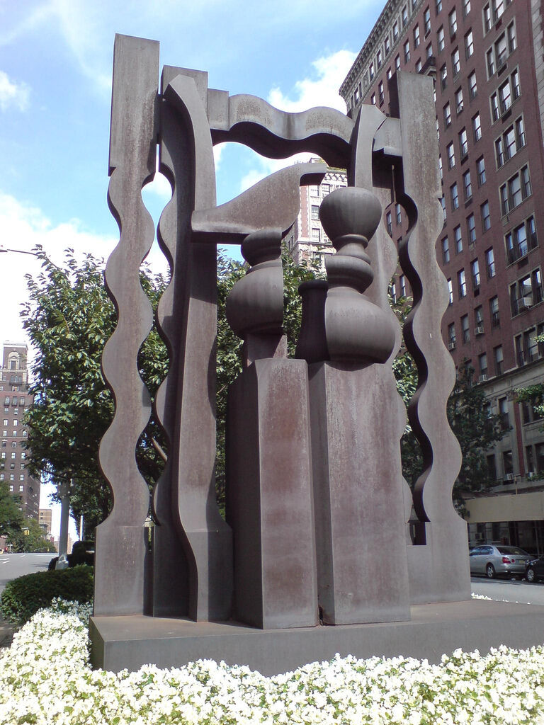 Large dark metal abstract sculpture with wavy pillars and rounded forms standing amid white flowers.