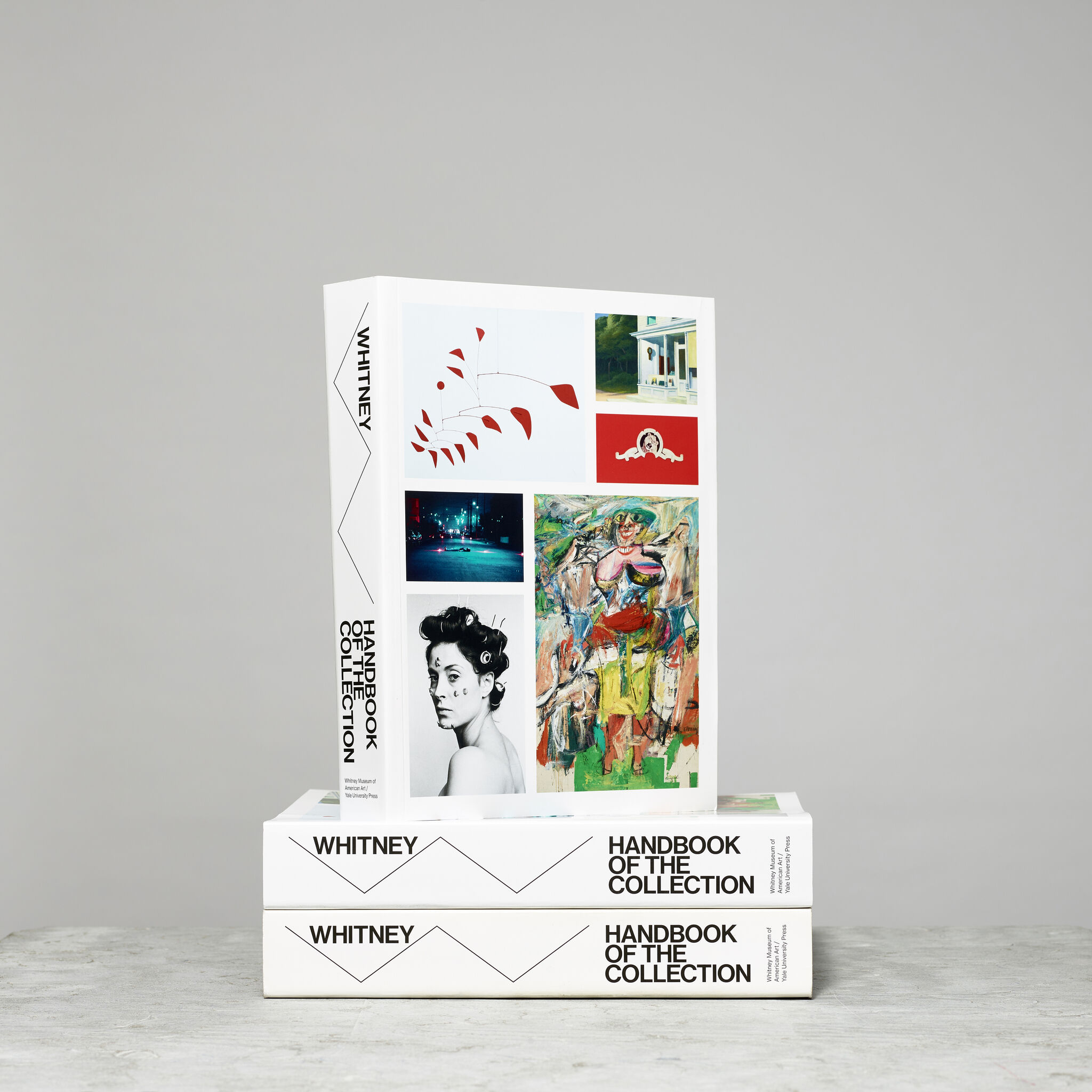 Stack of Whitney Handbook of the Collection books, with artworks on the front and the Whitney W on the spine.