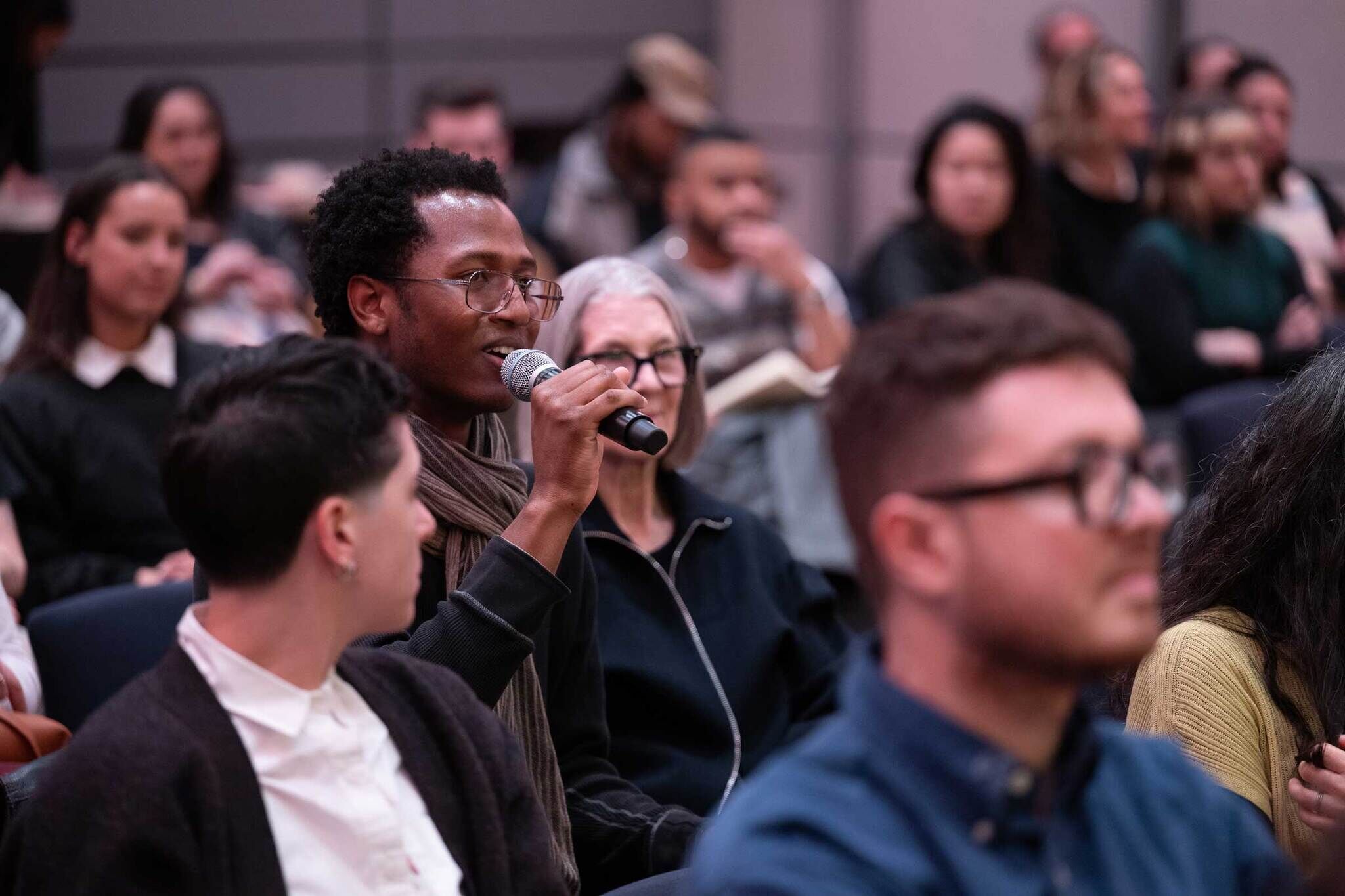A man with a microphone in his hand in a crowd asking a question.