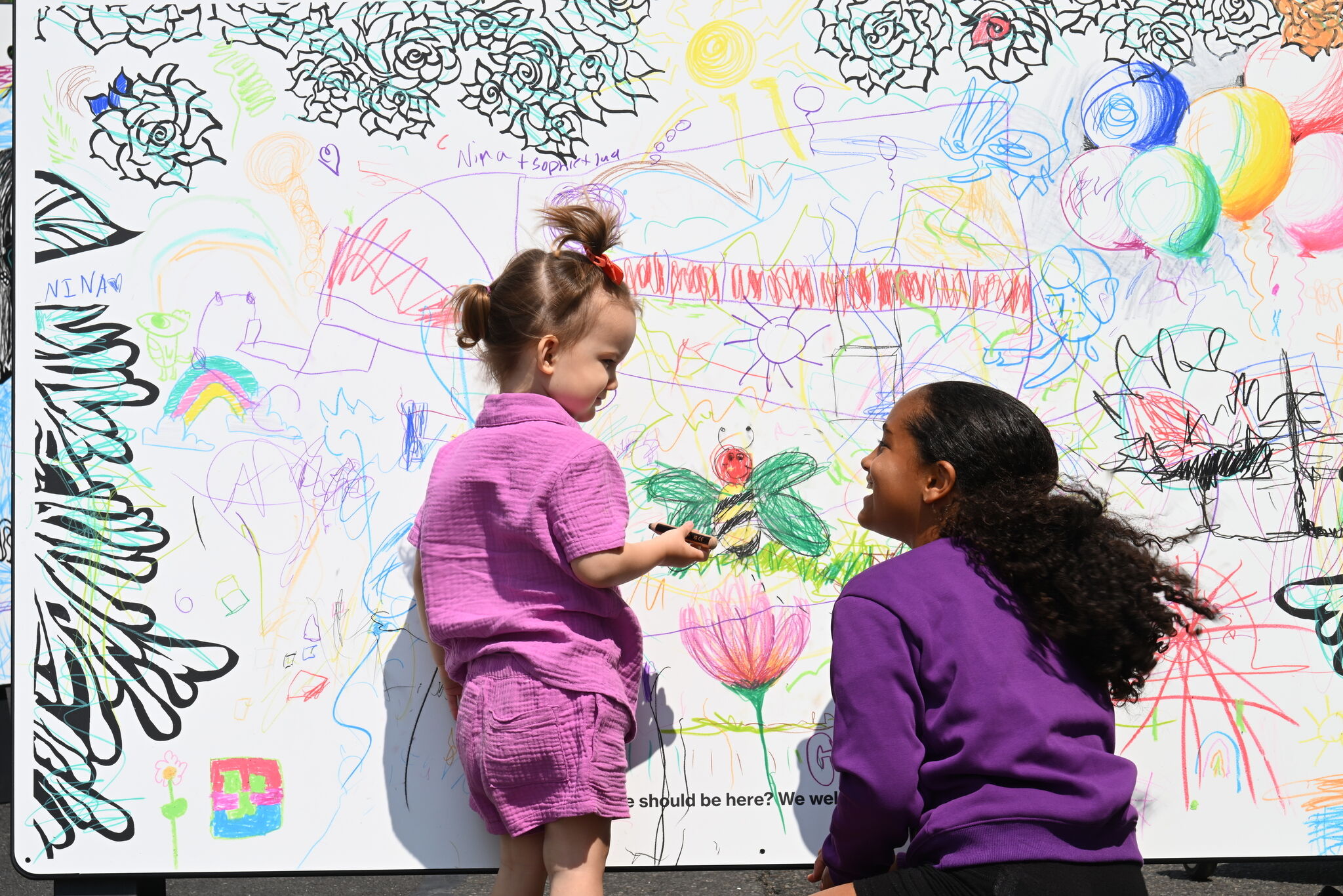 Pride celebration activity of two young children looking at each and smiling against a drawn backdrop.