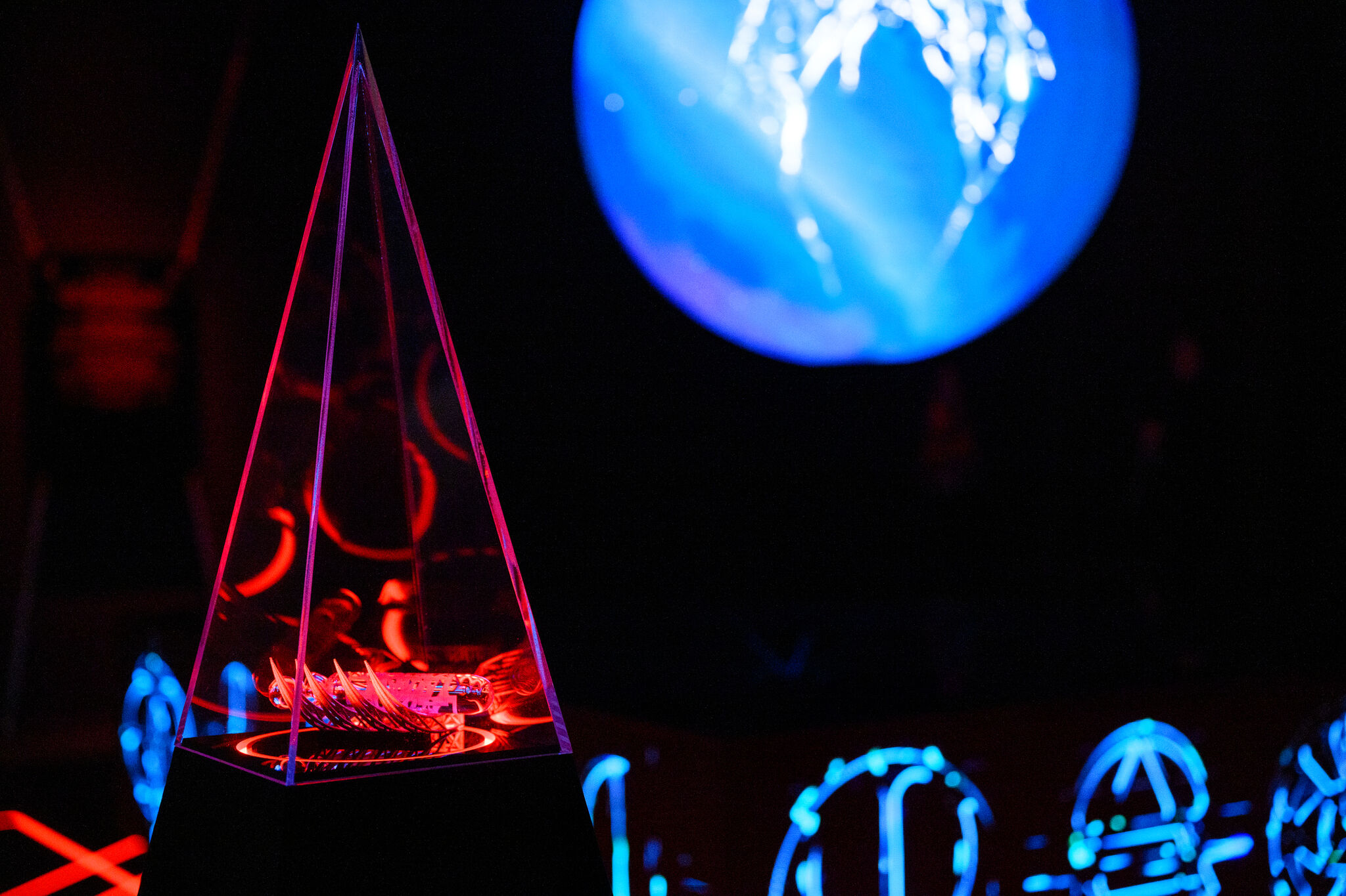 Close-up of a red-lit pyramid with a ghoulish hand holding a vial enclosed.