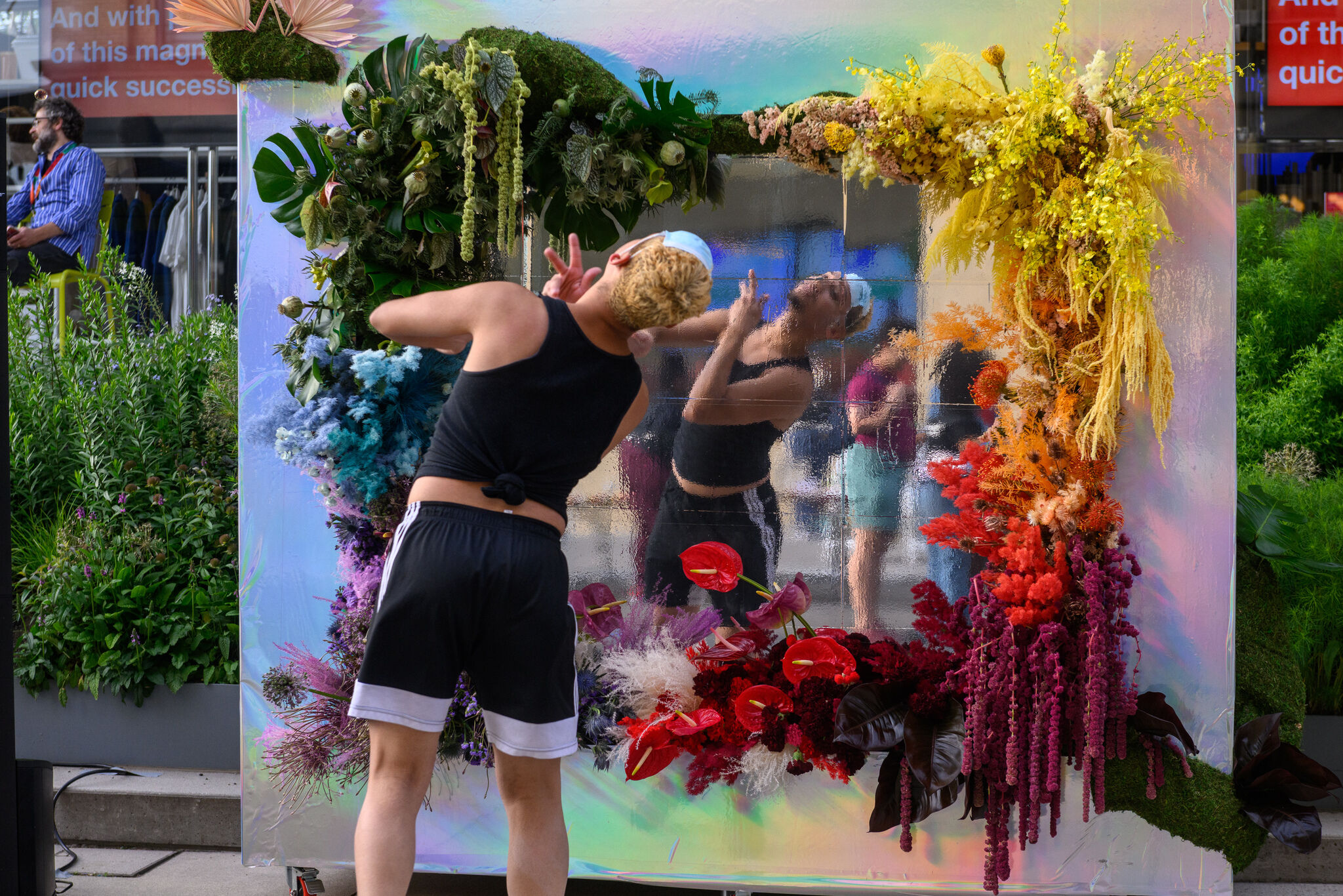 Performer in black shorts and tank top poses elegantly in front of a mirror adorned with multicolored flowers