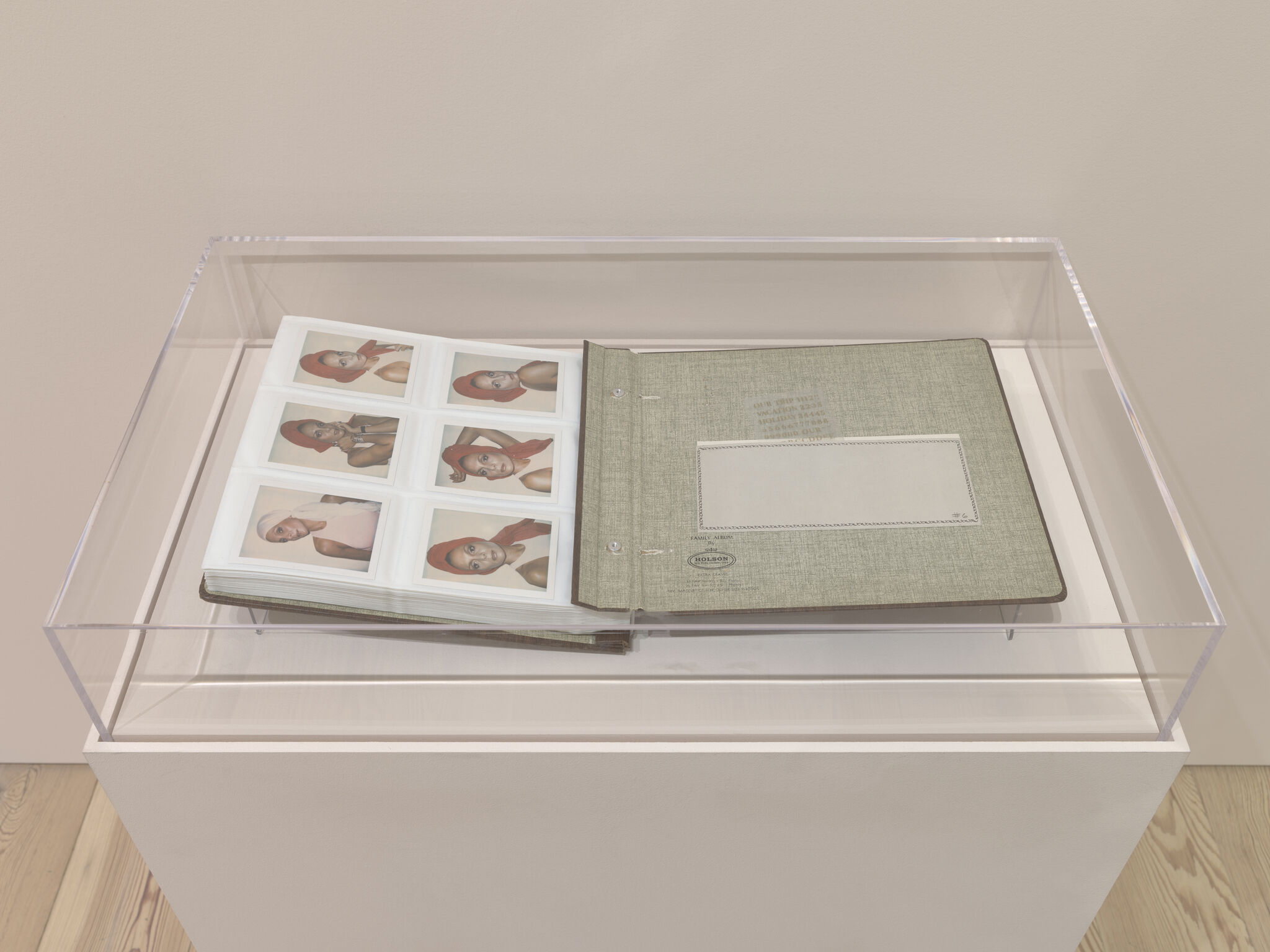 Photo album displayed in a glass case showing multiple Polaroid-style portraits of a woman in a red headscarf.