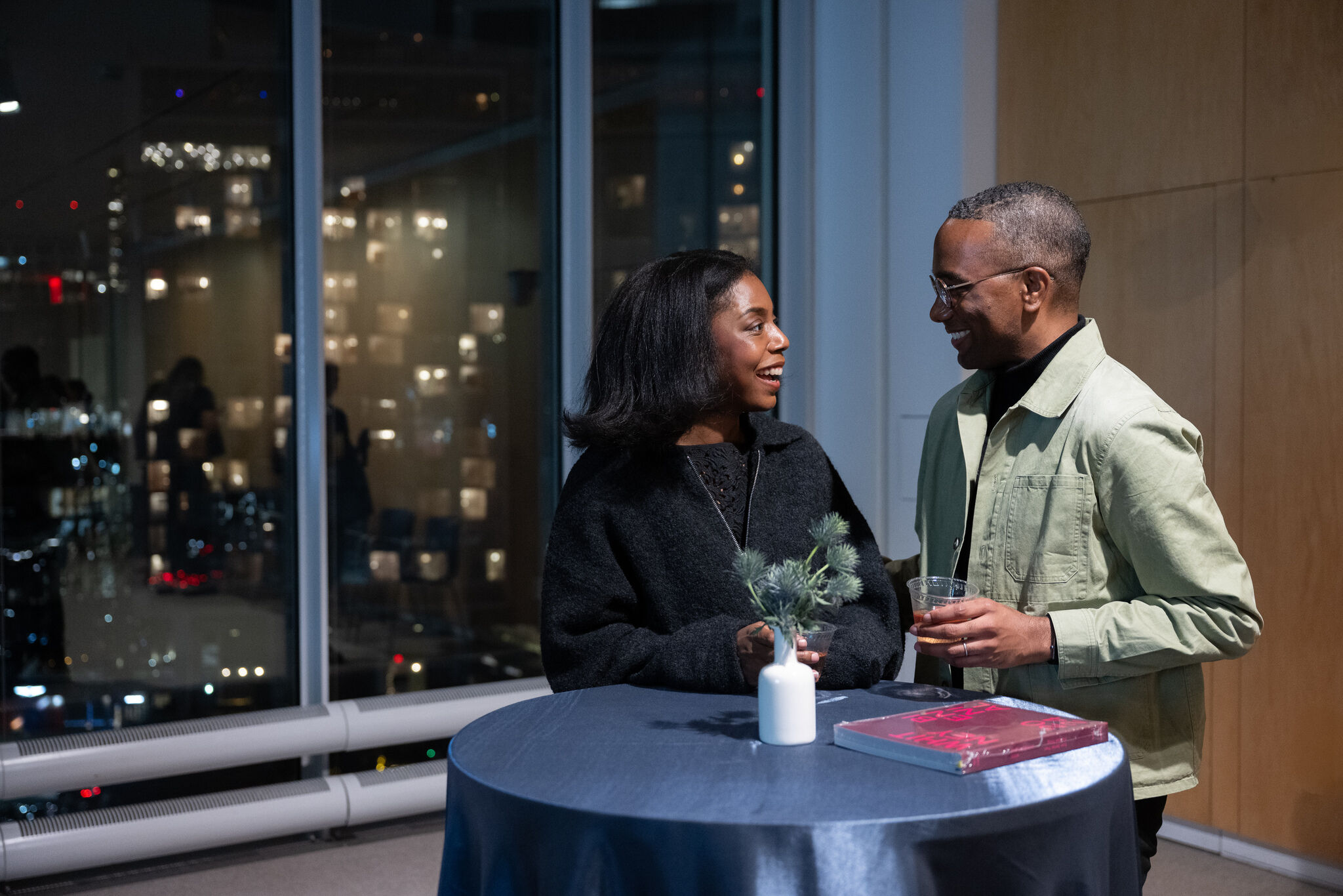 Whitney Contemporaries members raising a toast by a glass window with city views 