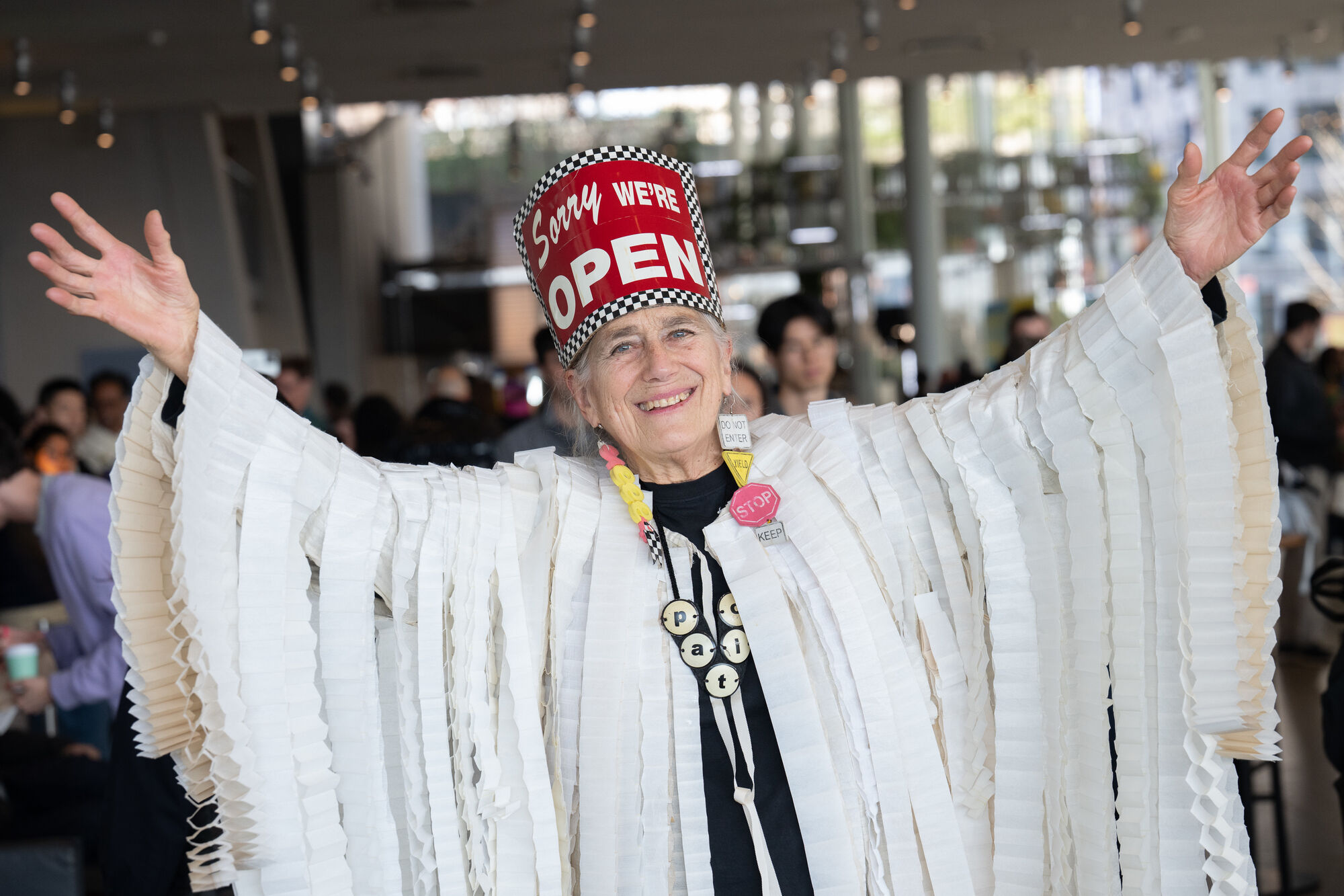 Woman wearing a red hat that says "OPEN" raises her arms while dressed in white fringe.
