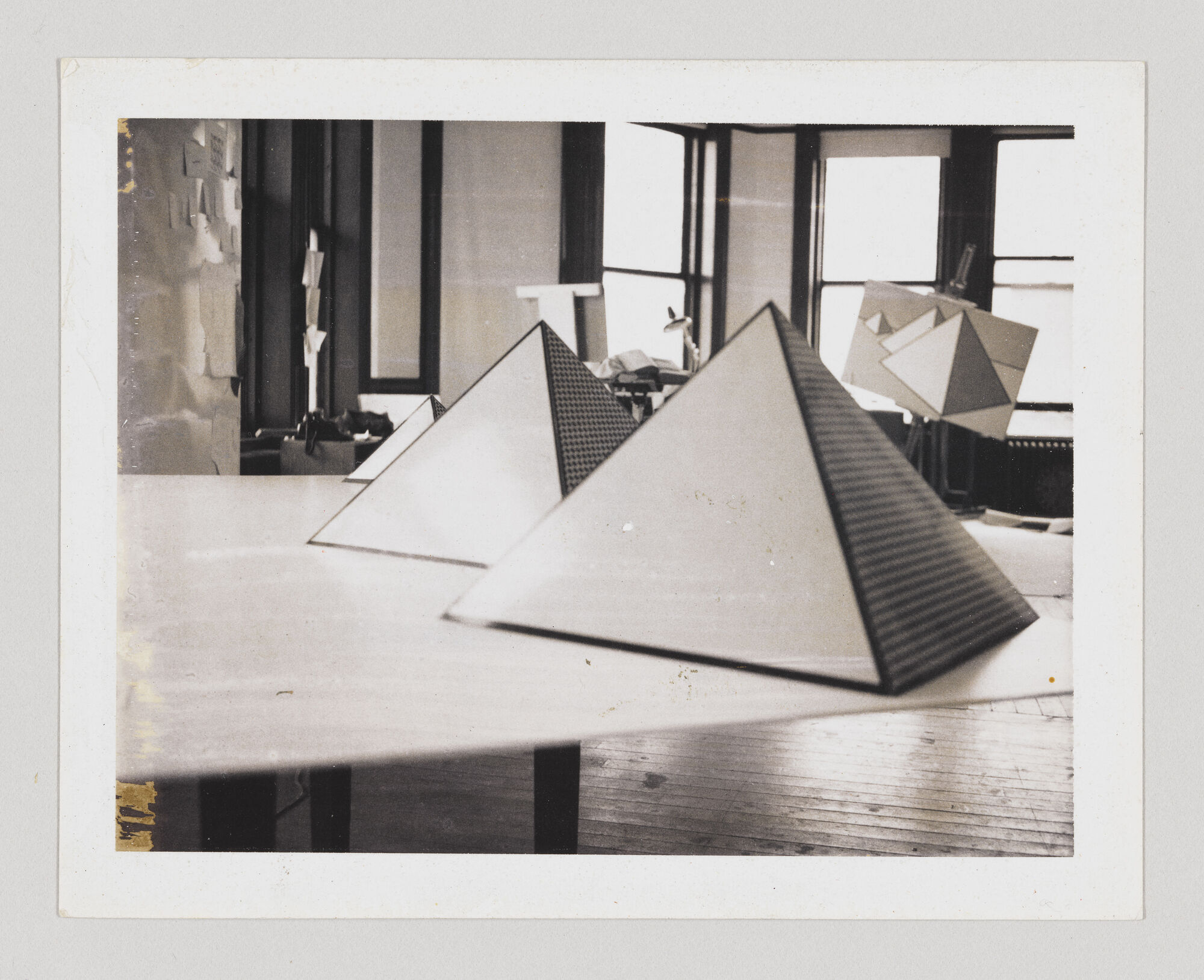 Several geometric pyramid models sit on a long table in a bright studio with tall windows.