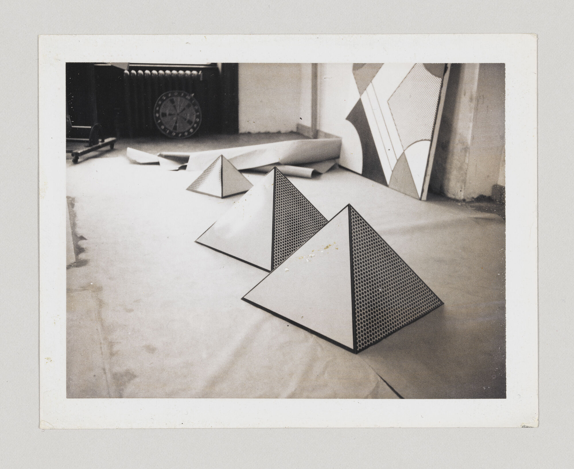 Three patterned paper pyramids arranged on a studio floor with rolled paper and a radiator.