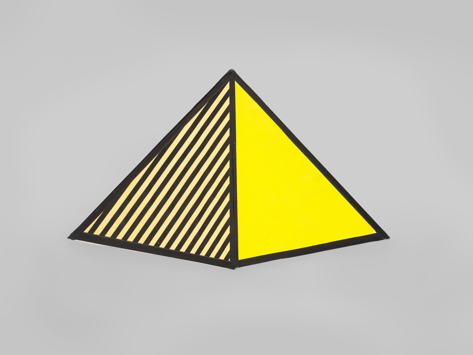A yellow triangular pyramid with one face solid yellow and the other face black-and-yellow diagonal stripes.