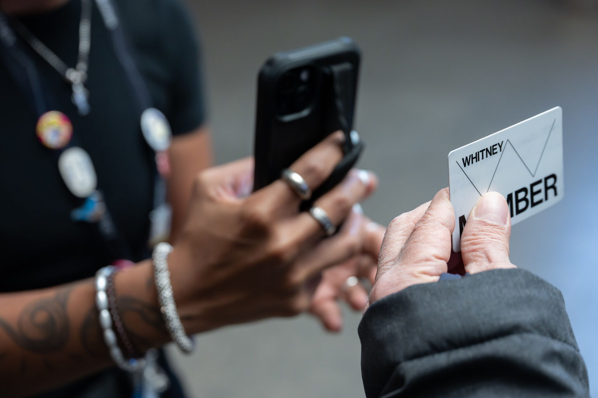 A staff member scans a Whitney membership card held by a visitor using a smartphone.