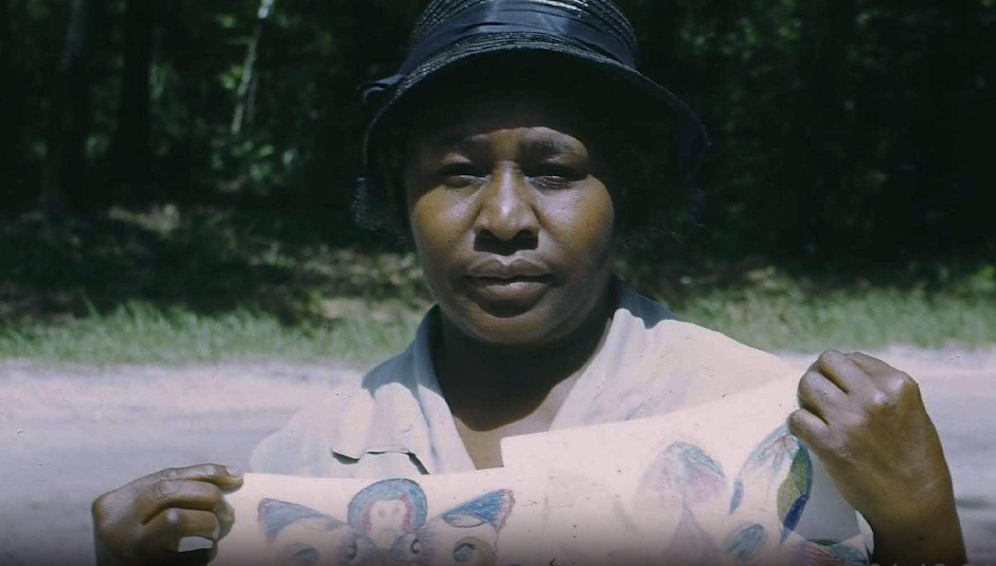 Minnie Evans in a black hat holding her work.