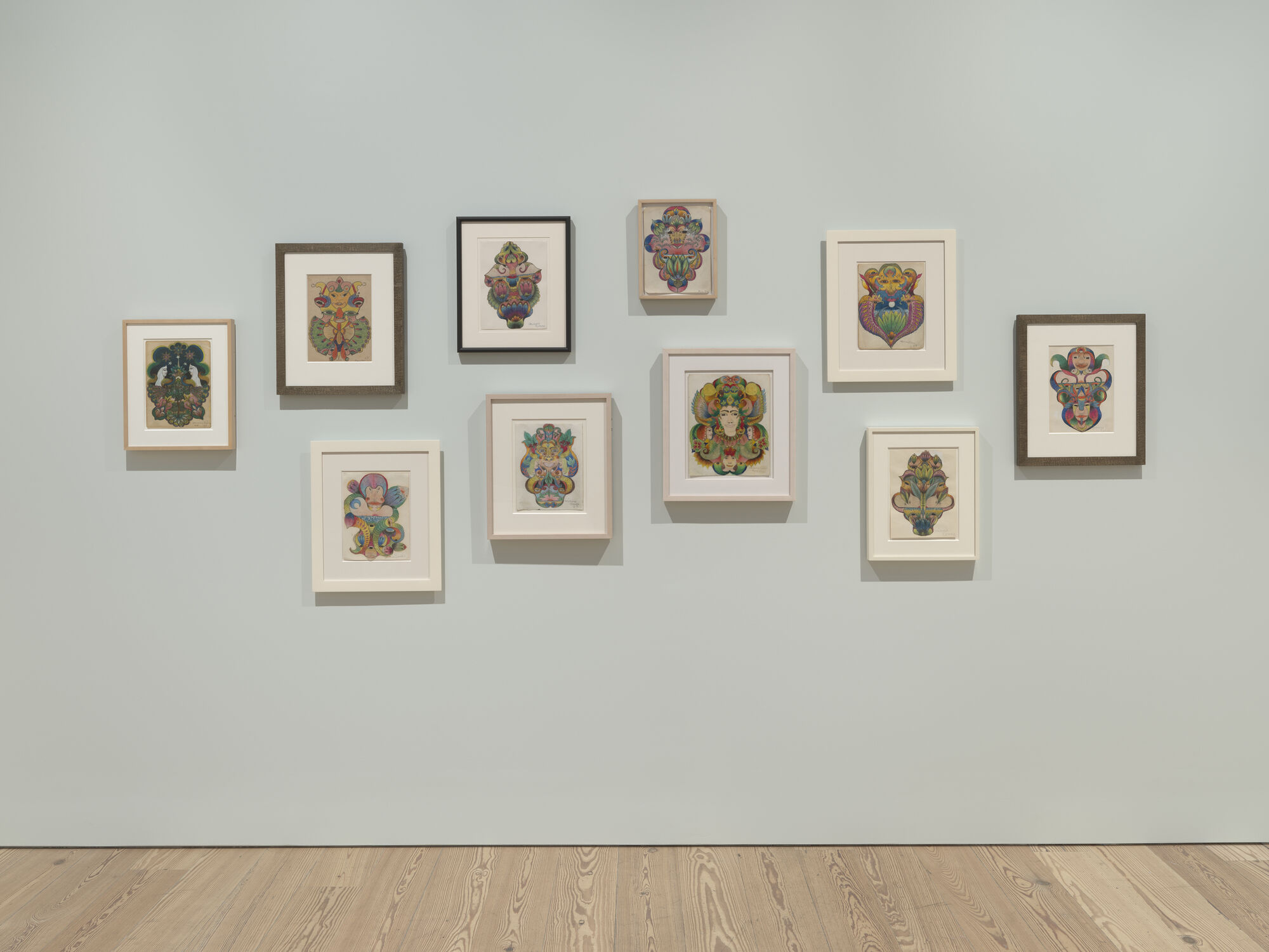 A group of colorful framed artworks arranged in a grid on a pale blue gallery wall.