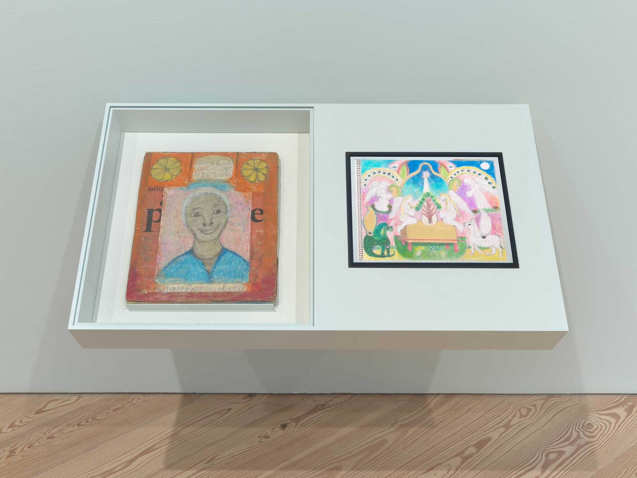 Two colorful framed drawings are displayed side by side in a white wall-mounted display case.