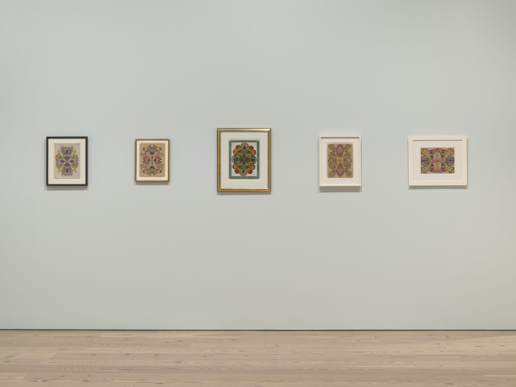 Five framed colorful abstract artworks hung in a row on a pale gallery wall.