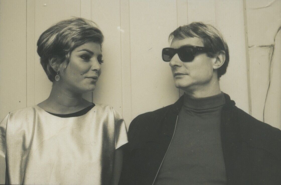 A woman looks toward a man wearing dark sunglasses and a coat.
