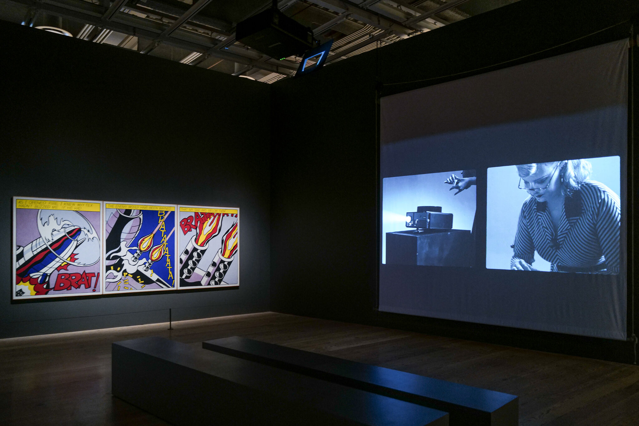 Comic panels brightly lit on the left wall while a black-and-white film is projected on the right.