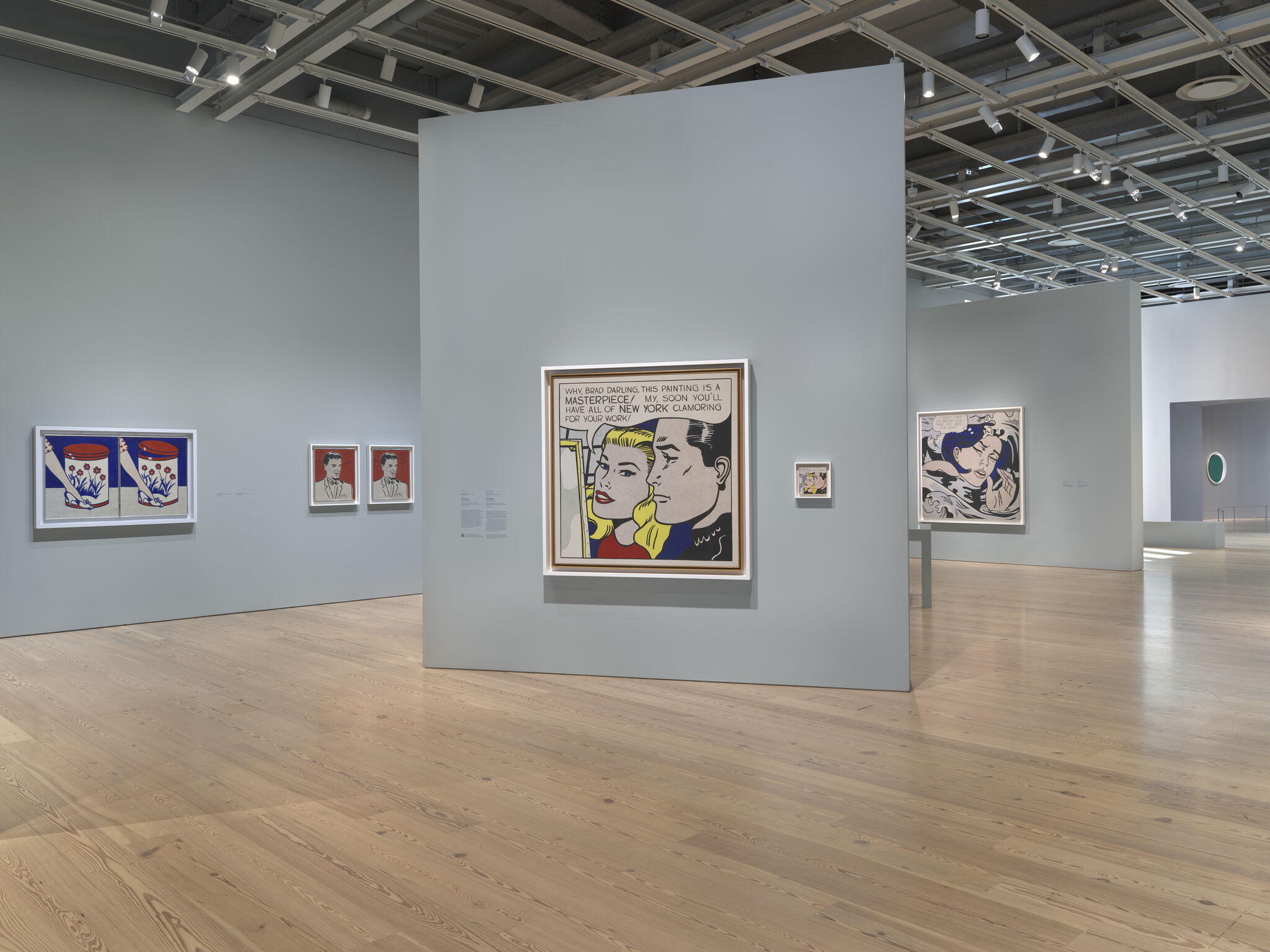 Museum gallery with pale blue walls displaying large pop-art comic-style paintings and framed prints.