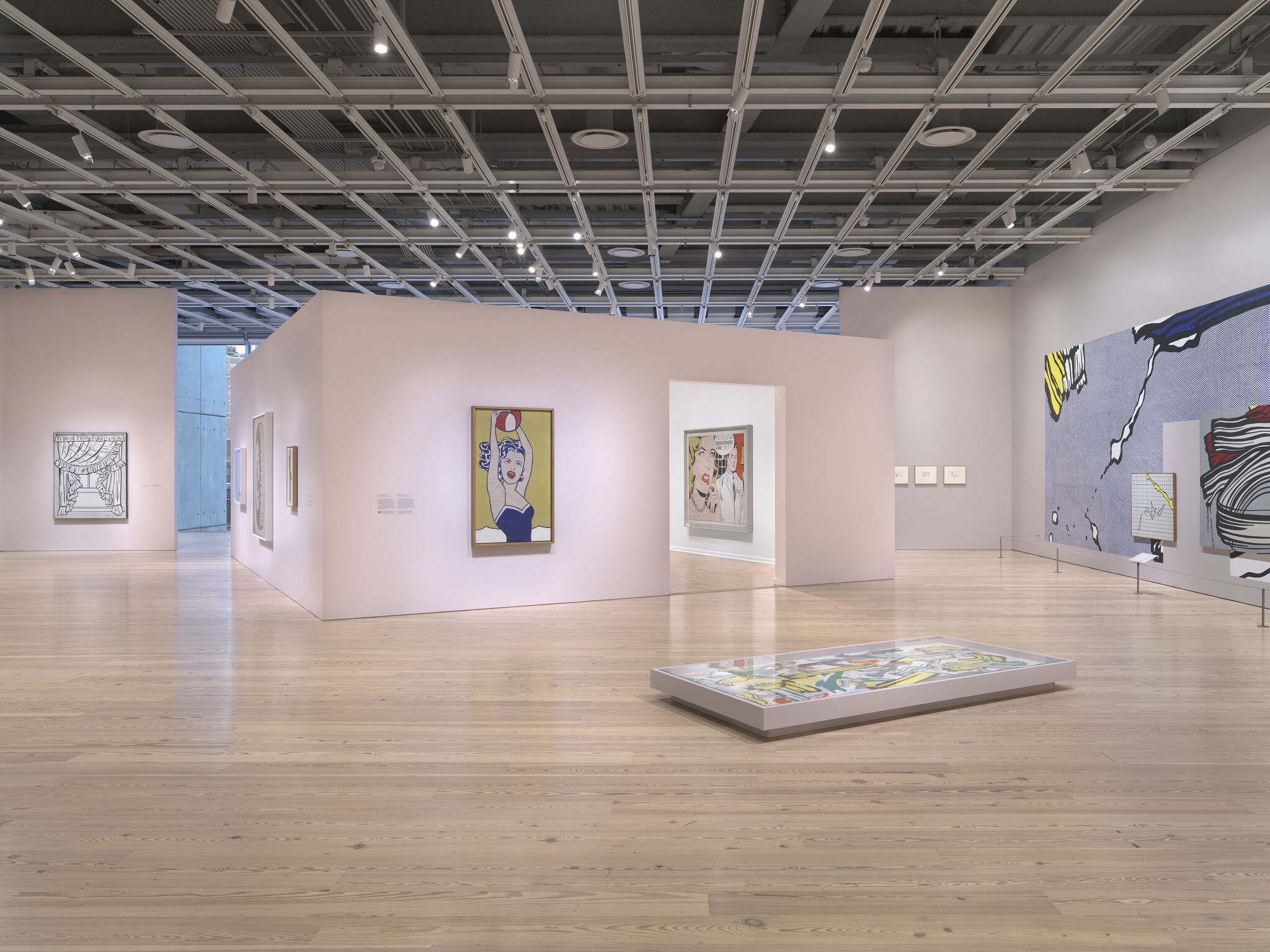 Spacious modern art gallery with pink partition walls displaying colorful pop art paintings and wood floors.